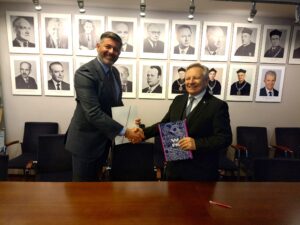 Dwóch mężczyzn podaje sobie ręcę na tle ściany z portretami