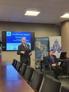 Dwóch mężczyzn, jeden stoi i przemawia, drugi siedzi na krzesle. W tle Telebim z napisem L Wiedzy Technicznej, oraz dwa rollupy - NOT i SEP.