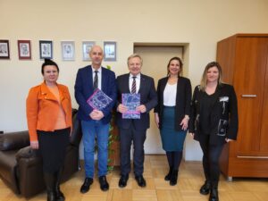 5 osób - 2 mężczyzn i 3 kobiety - stoją na tle ściany. Mężczyźni trzymają w dłoniach kolorowe teczki