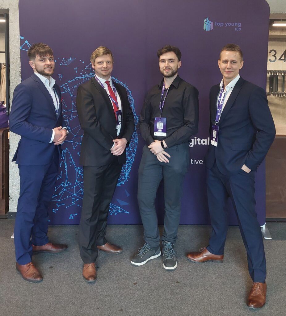 Czterech uśmiechniętych, elegancko ubranych mężczyzn pozuje na tle granatowej ścianki do zdjęcia