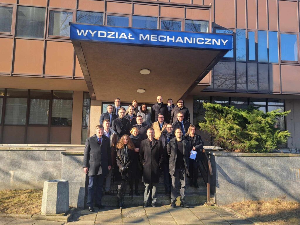 Grupa kilkunastu osób pozuje do zdjęci na tle wejścia głównego do budynku A na kampusie Wydziału Mechanicznego Politechniki Krakowskiej