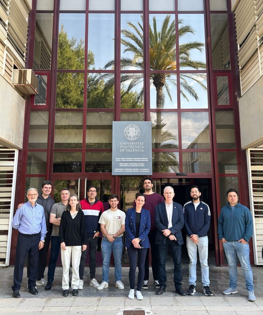 Grupa uśmiechniętych osób pozuje do zdjęcia na tle budynku z napisem Universitat Politecnica de Valencia