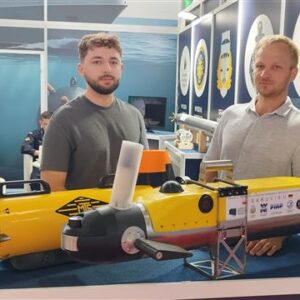 Dwóch mężczyzn stoi za podwodnym robotem autonomicznym w kolorze żółtym.