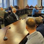 przy stole siedzący ludzie, słuchają wystąpienia